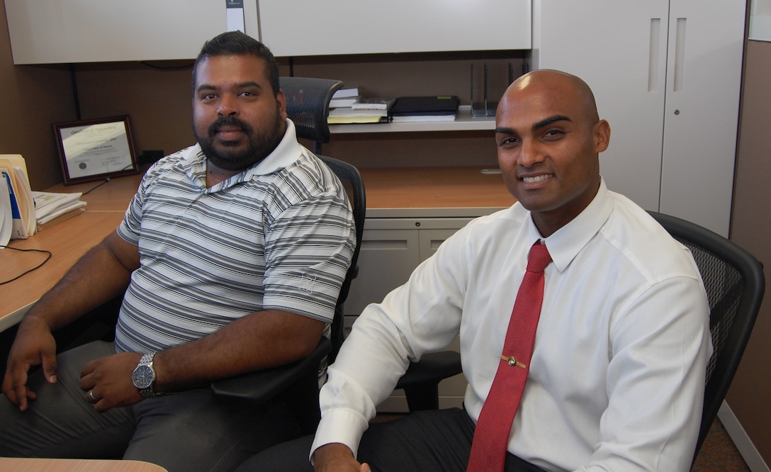 Two males, one in a short-sleeved shirt, and the other one in a long-sleeved shirt and tie, smile at the camera.