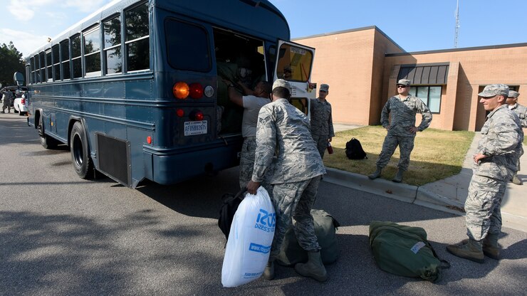 Airmen load bags of ice on the back of a bus.
