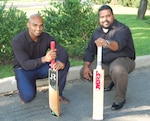 Two men, both holding their cricket bat, kneel to the ground.