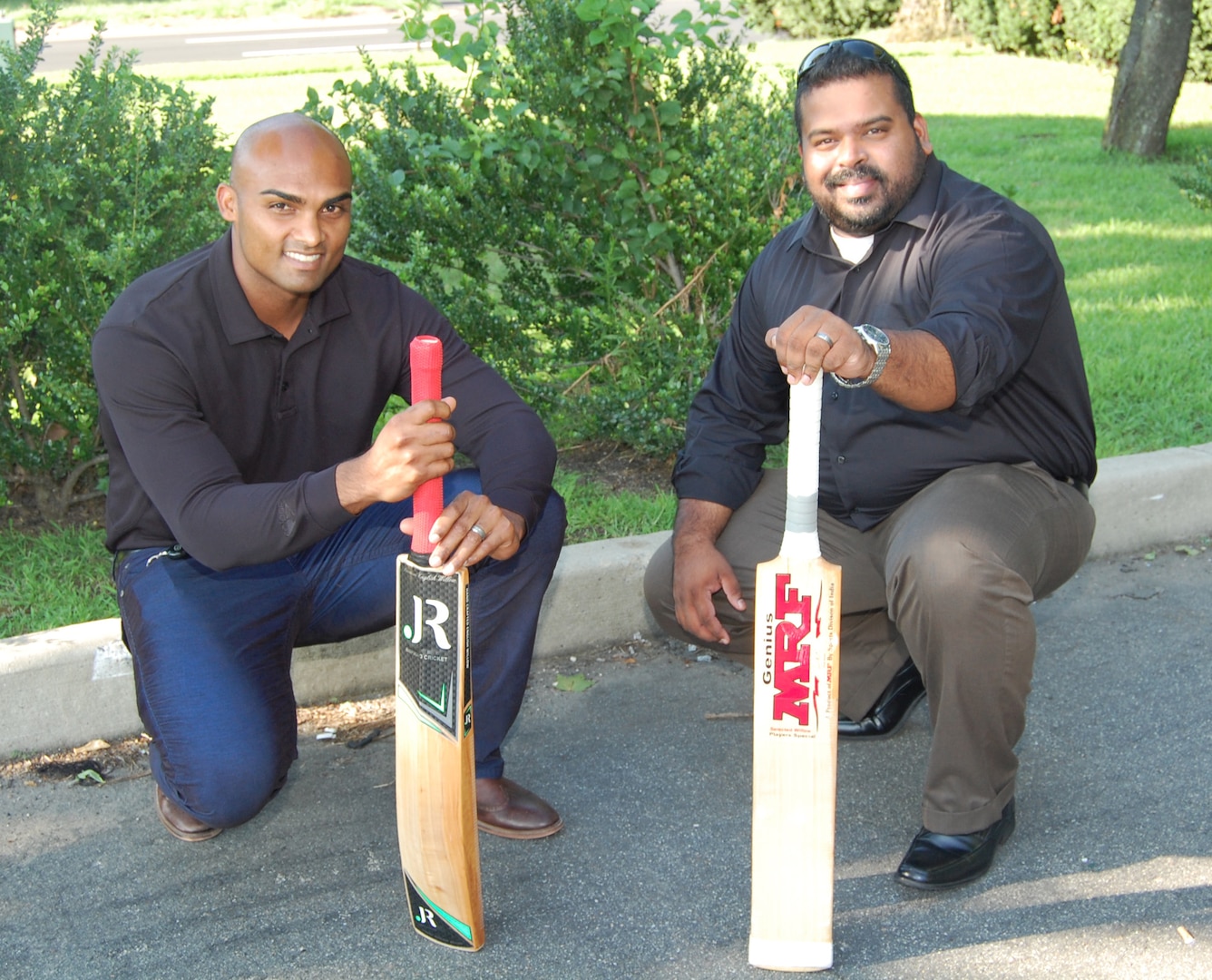 Two men, both holding their cricket bat, kneel to the ground.