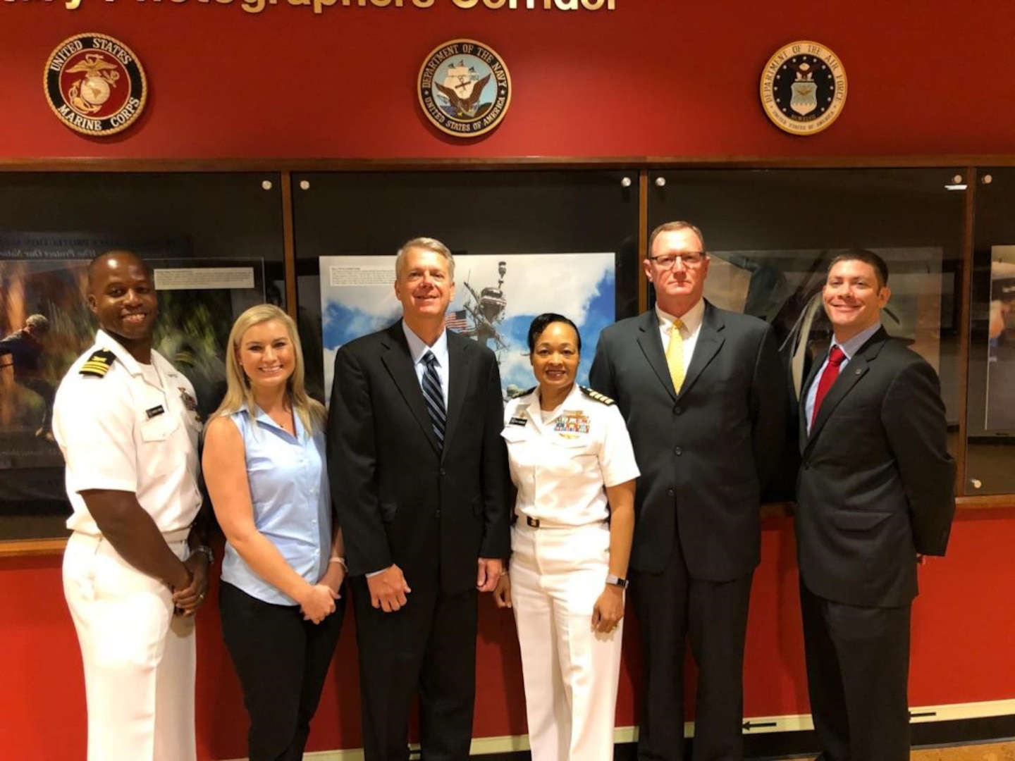 Group photo of military and civilian personnel standing in front of an exhibit at the Pentagon