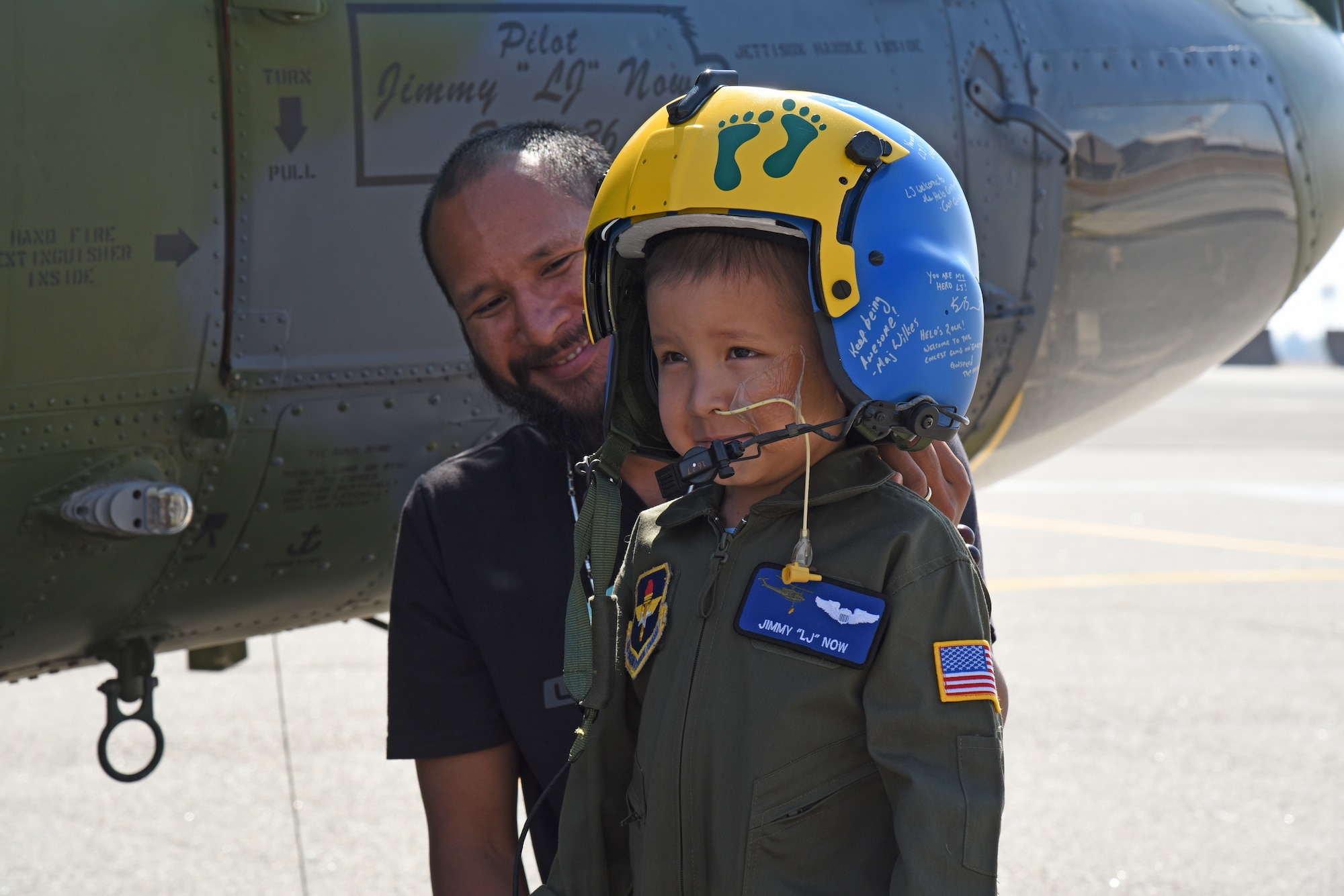 Jimmy Now helps Jimmy "LJ" Now try on his personalized helmet given to him by the 36th Rescue Squadron during his visit Sept. 7, 2018, at Fairchild Air Force, Washington. Following military tradition, the 36th also provided LJ with a call sign, painting his name and “Blade 36” on the door of the helicopter. (U.S. Air Force photo/Staff Sgt. Mackenzie Mendez)