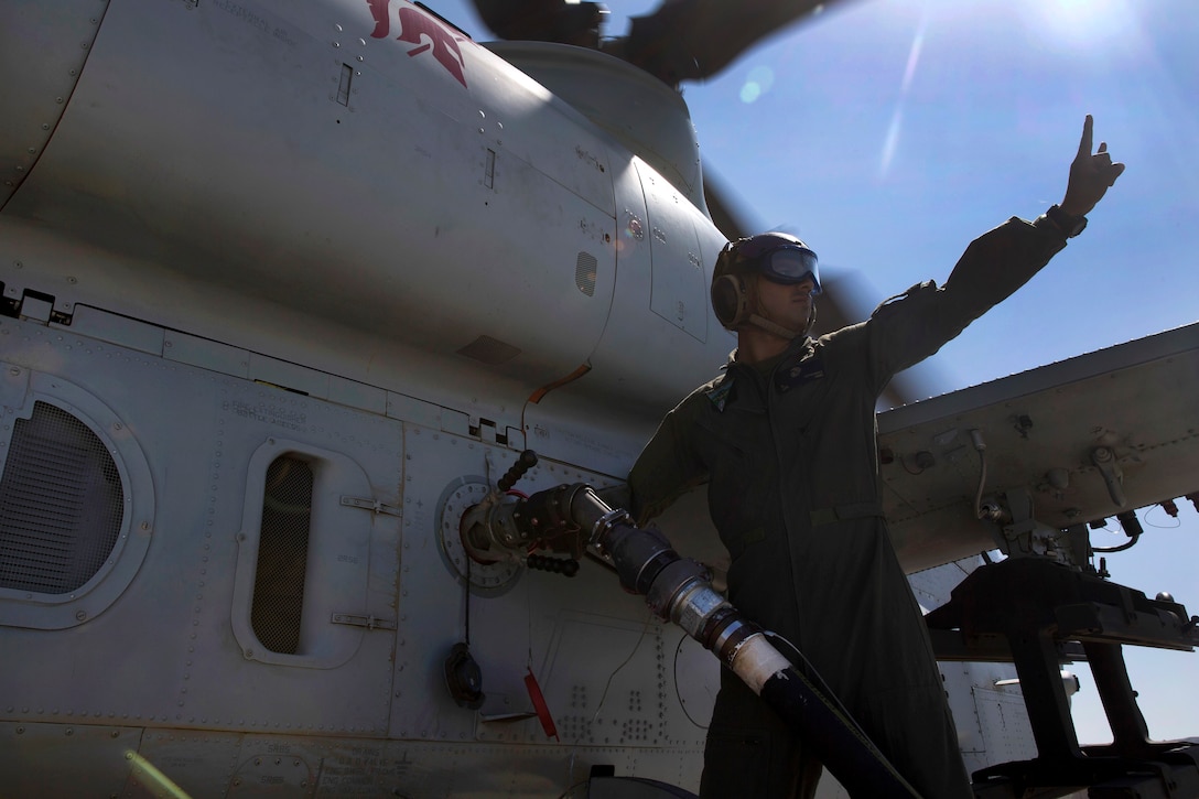A Marine signals to another Marine while refueling a helicopter.