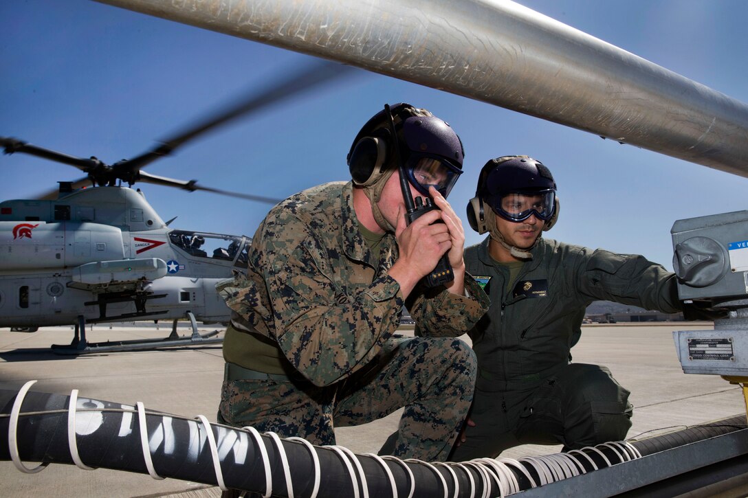 Marines radio the fuel dispatcher while refueling a helicopter.