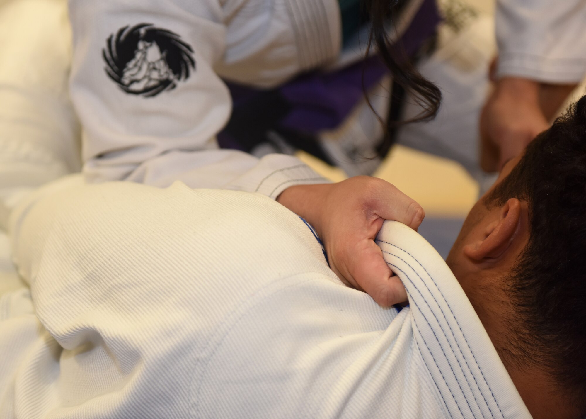 People in white uniforms practice martial arts on a  blue mat.