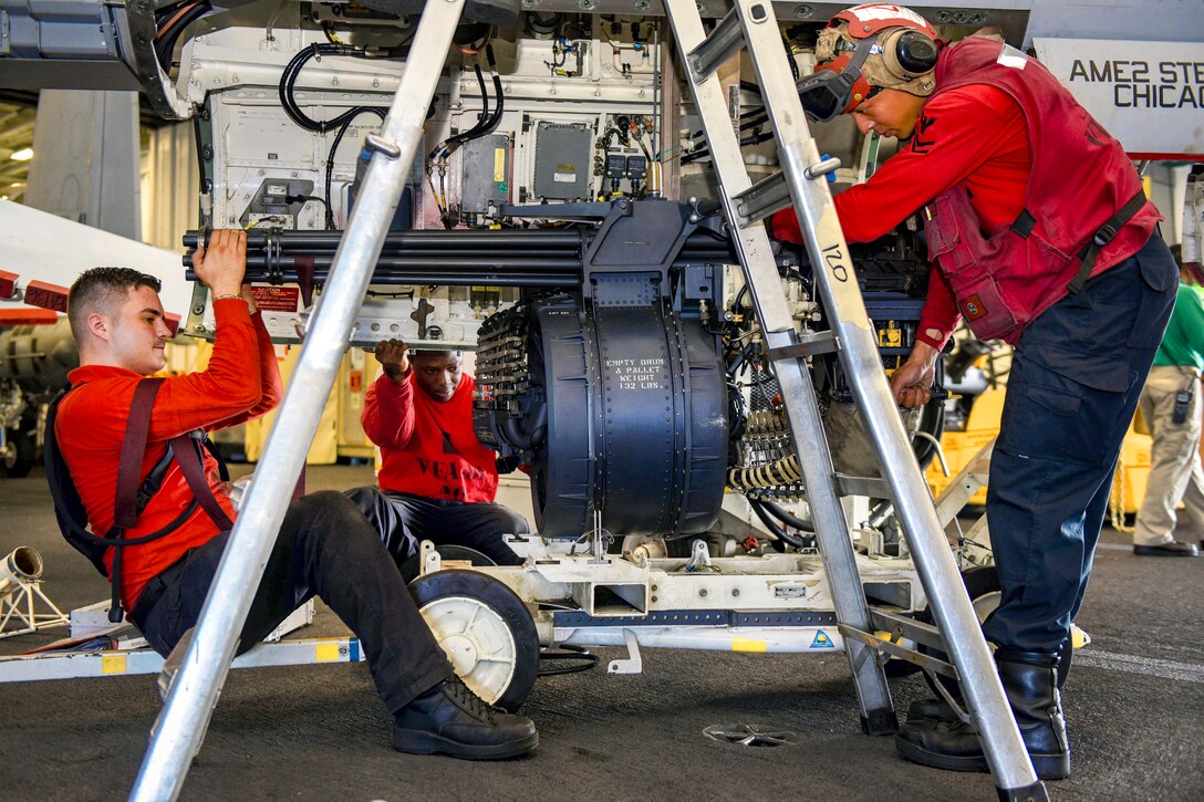 Sailors remove a machine gun from an F/A-18E Super Hornet.