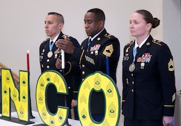 Master Sgt. Jerome Simmons Jr., center, 1st Theater Sustainment Command, lights a white candle during the 1st TSC NCO induction ceremony March 2, 2018 at Fort Knox Ky., as 1st Sgt. Paul Gomez, first sergeant, Headquarters and Headquarters Company, 1st Special Troops Battalion, 1st TSC, and Sgt. 1st Class Kerrilee Case, maintenance manager, 1st TSC, looks on. Each candle has a symbolic meaning, with white representing honesty and integrity, red representing valor, and blue representing vigilance and honor.