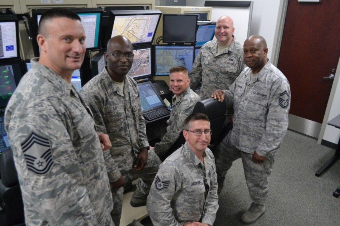 Six members of the Pennsylvania Air National Guard's 111th Operations Support Squadron stand in a room next to an MQ-9 Flight Simulator.