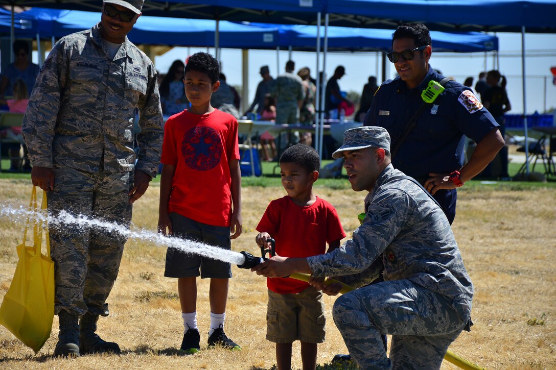 A firefighter from the 349th Civil Engineers Squadron helps a military child use a fire hose during Operation Family Circles at Tavis Air Force Base, Calif., on Sept. 8, 2018. The 349th Air Mobility Wing hosted OFC where families could experience a variety of demonstration booths, activities, and foo