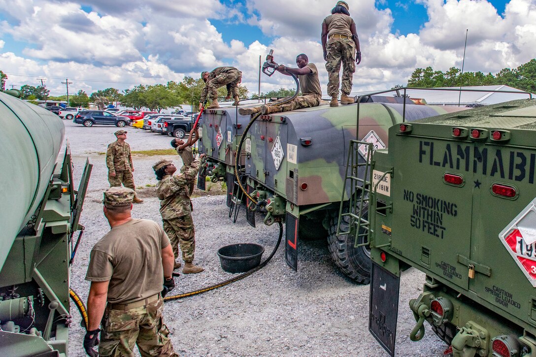 Service members transfer fuel between large storage containers.