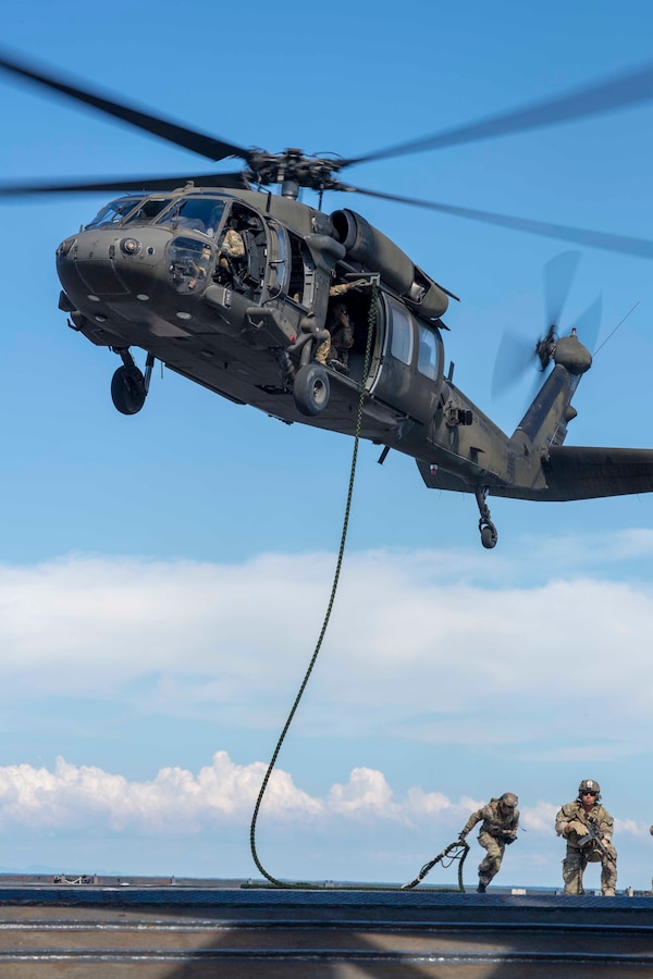 U.S. Soldiers fast-rope from a helicopter onto the flight deck of the USS Gunston Hall.