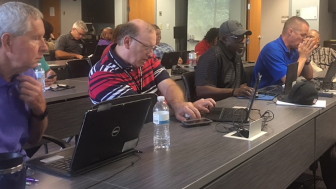 Group photo of employees sitting behind a table looking at their laptops