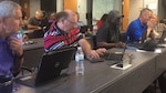 Group photo of employees sitting behind their table looking at their laptops