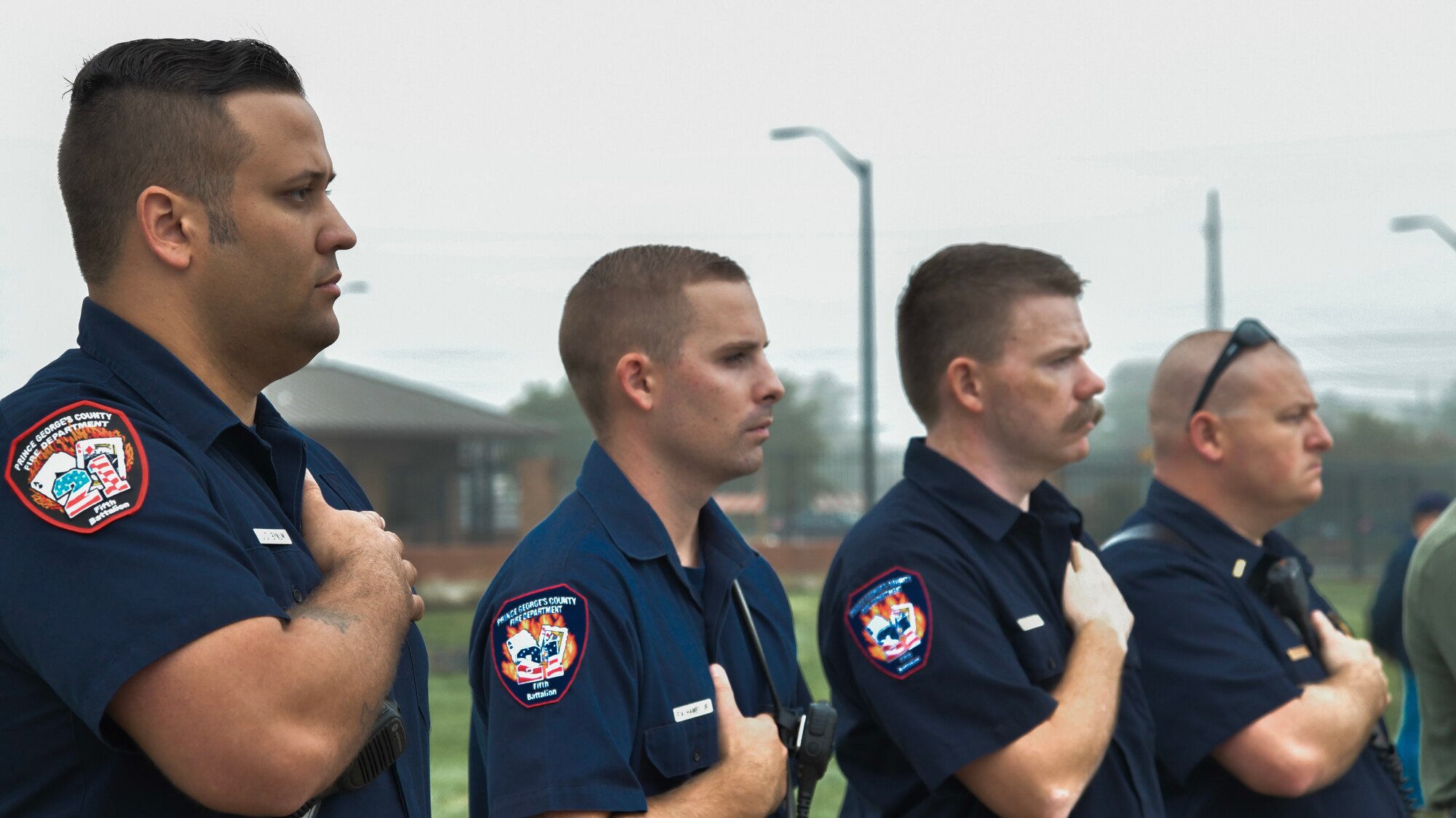 Members of the Oxen Hill Volunteer Fire Department in Oxen Hill, Maryland, pay respect as “Taps” plays during the 9/11 Memorial Service on Joint Base Andrews, Md., Sept. 11, 2018. Fire fighters with the OHVFD attended the ceremony after setting up the American flag between two fire trucks.
