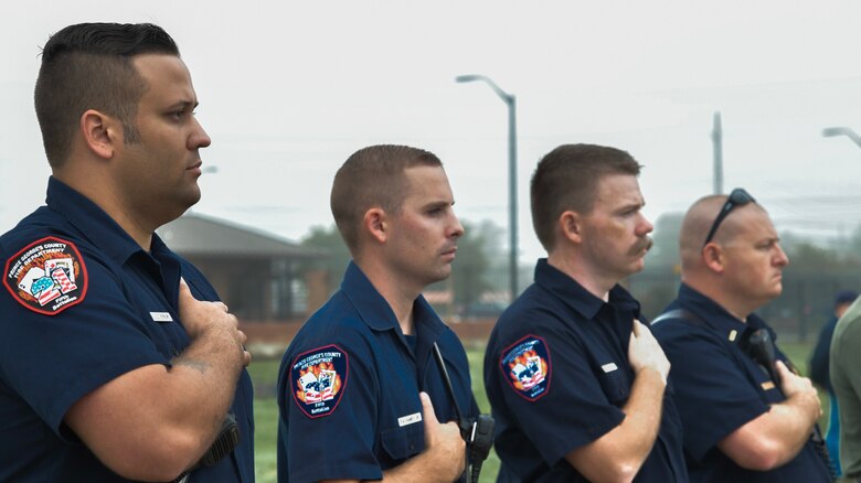 Members of the Oxen Hill Volunteer Fire Department in Oxen Hill, Maryland, pay respect as “Taps” plays during the 9/11 Memorial Service on Joint Base Andrews, Md., Sept. 11, 2018. Fire fighters with the OHVFD attended the ceremony after setting up the American flag between two fire trucks.