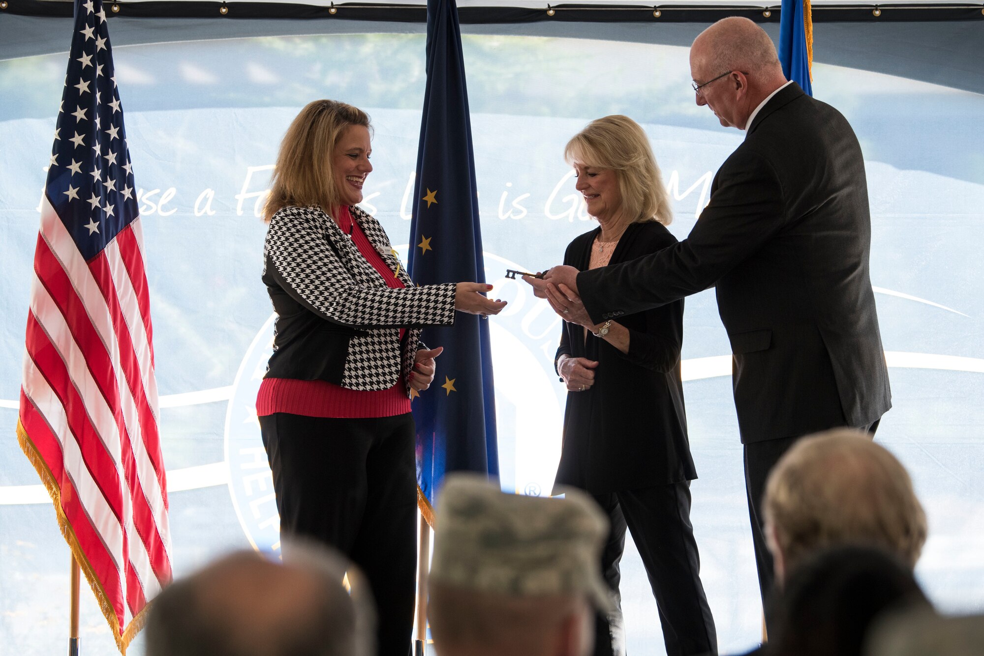 Jenny Hall, Fisher House manager, receives the key for Fisher House II during the opening ceremony at Joint Base Elmendorf-Richardson, Alaska, Sep. 10, 2018. The Fisher House program is a network of comfort homes where families can stay at no cost while a loved one is receiving treatment. The need for another house was so great in Alaska, the foundation funded the building of the second Fisher House. Fisher House II features a two-story building with more than 14,000 square feet – 16 suites which include a private bedroom and bath, a shared family room, living room, and common kitchen, and laundry facilities for families.