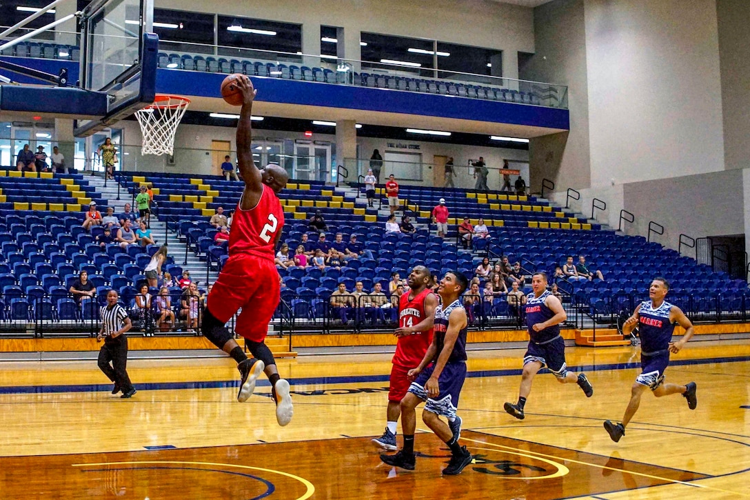 A basketball player jumps to make a shot as others watch on an indoor court.