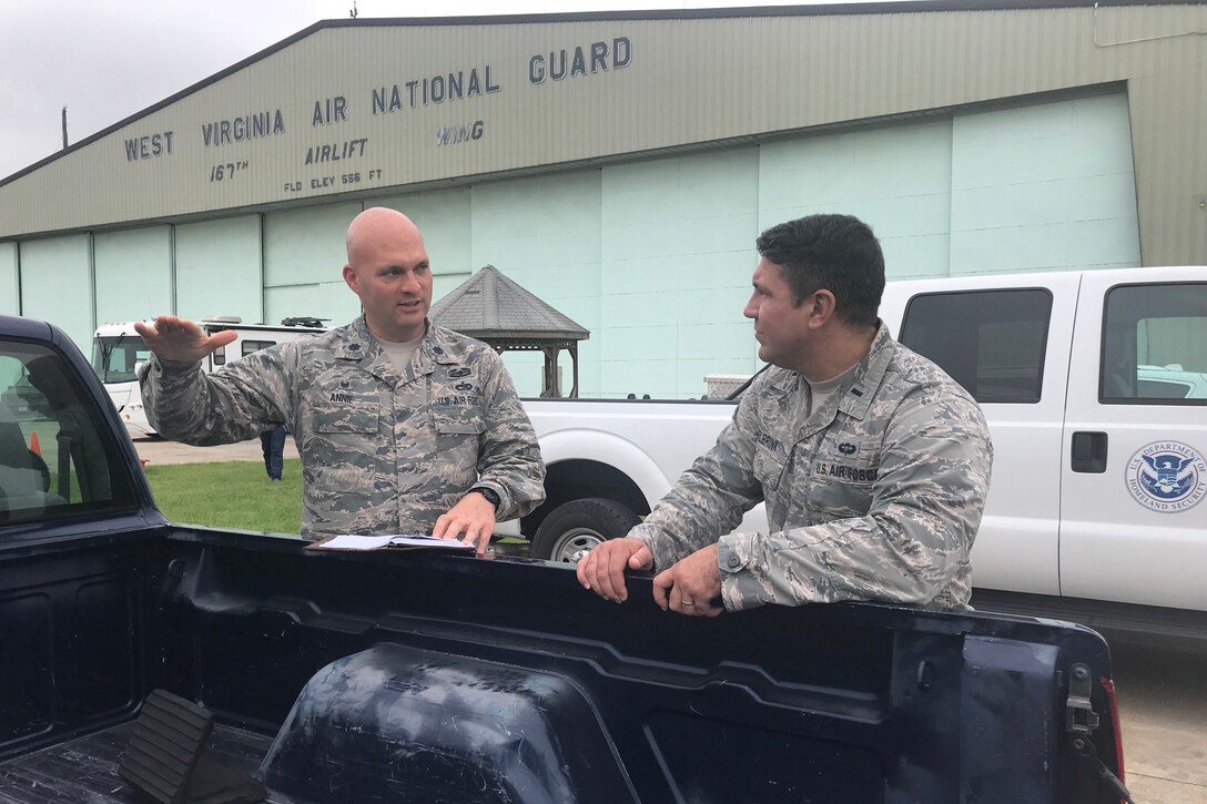Two airmen talk standing next to a pickup truck.