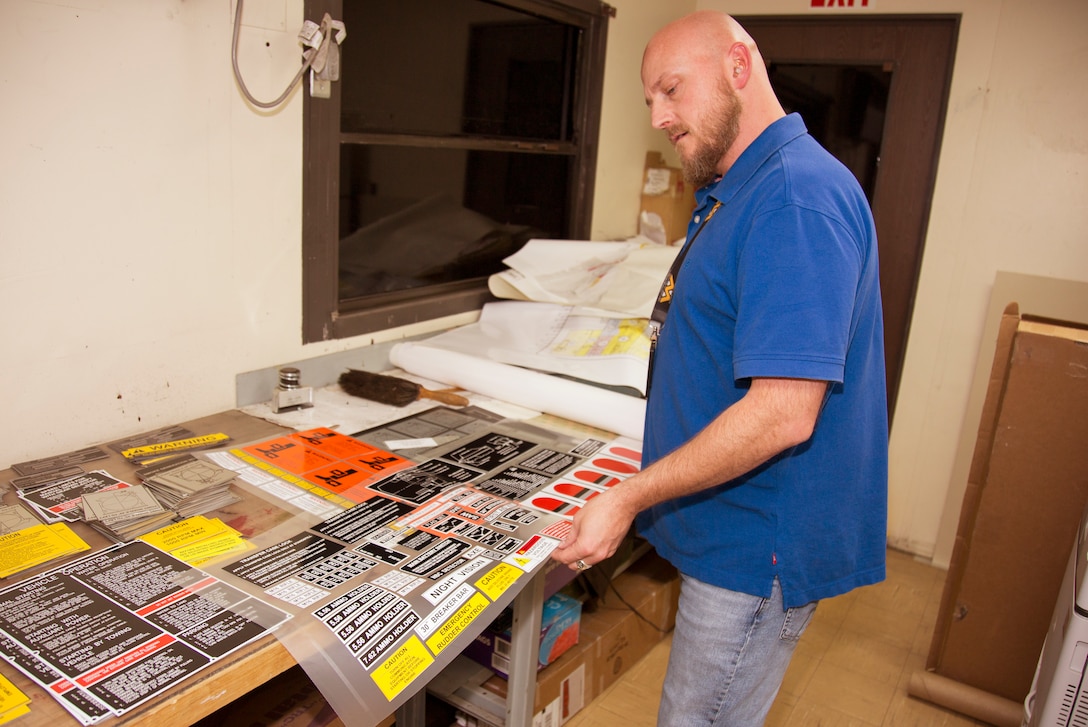 Schyler Yacono, supervisor, Test, Measurement, and Diagnostic Equipment Department, displays a sheet of decals printed and cut on a thermal vinyl printing machine. The sheet, or kit, of decals is used on one vehicle being refurbished at Production Plant Barstow, Marine Depot Maintenance Command, Sept. 4.