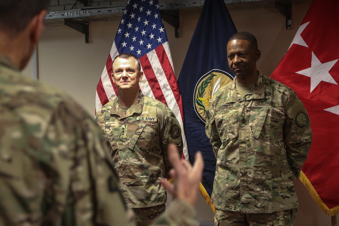Army Lt. Gen. Paul E. Funk II, outgoing commanding general of Combined Joint Task Force Operation Inherent Resolve, left, and Army Command Sgt. Maj. Michael A. Crosby Jr., stand together while Army Gen. Joseph L. Votel, commander of U.S. Central Command, gives a speech as part of a military decorations ceremony in Baghdad.