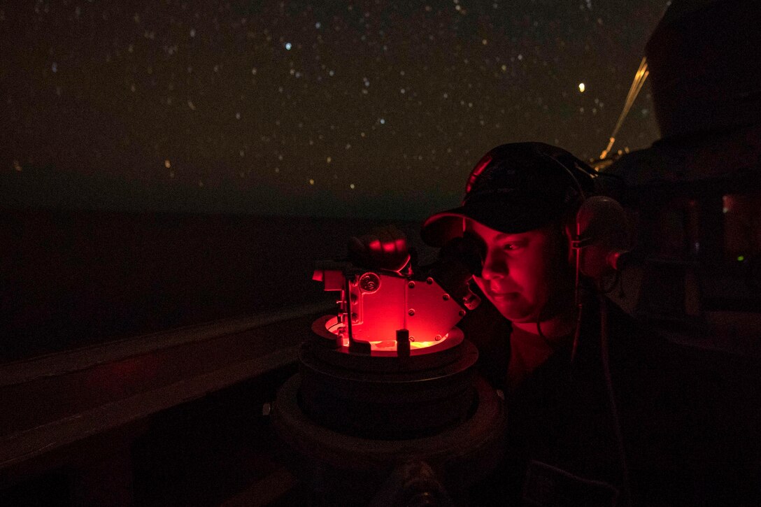 A sailor consults navigation equipment under the night sky.