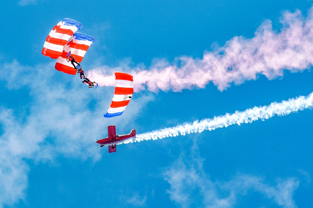 Veterans using American flag parachutes descend through the sky.