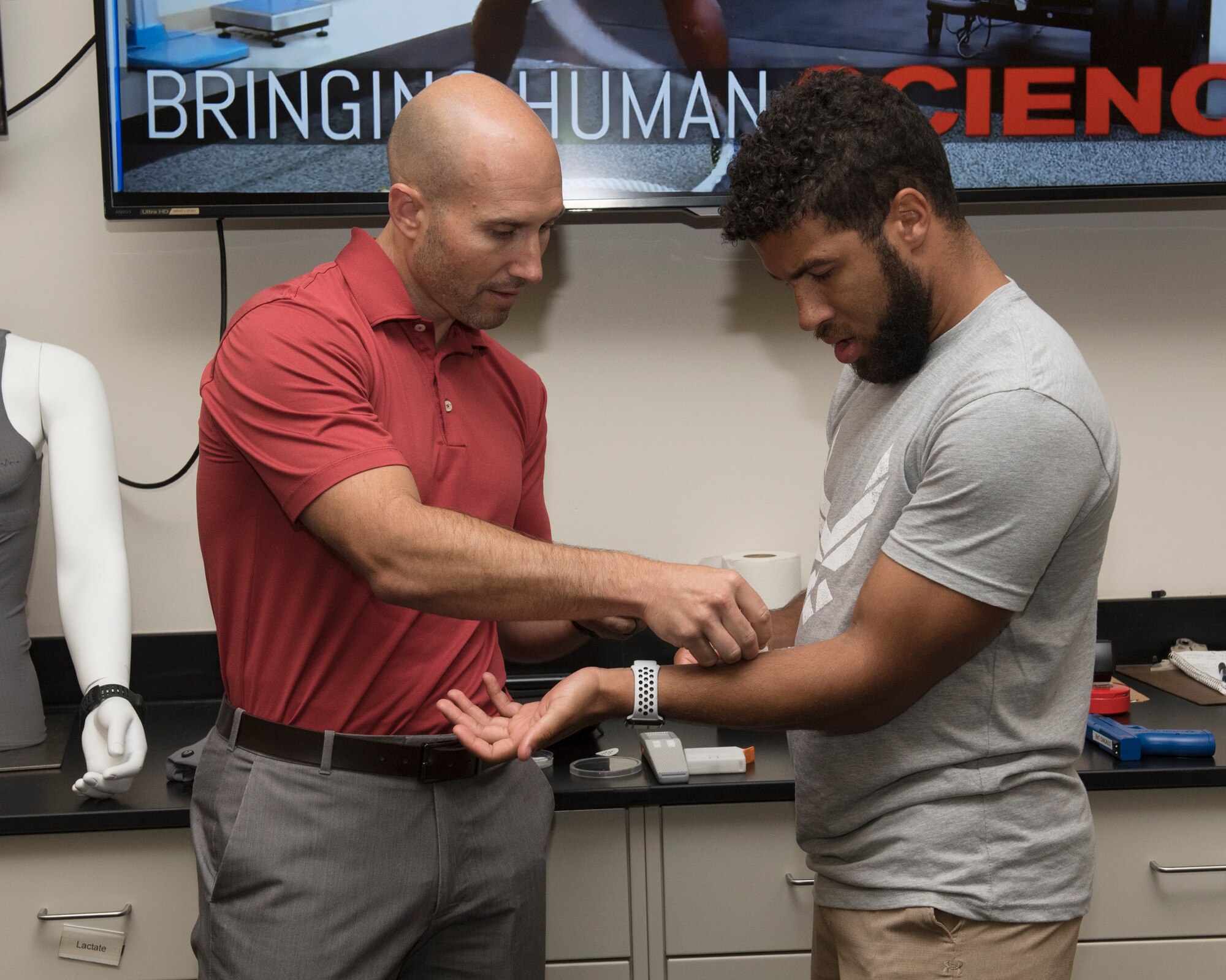Dr. Adam Strang, 711th Human Performance Wing scientist, applies a sweat sensor patch on NASCAR driver, Darrell “Bubba” Wallace Jr. as part of a demonstration on his tour inside the Strong Lab at the U.S. Air Force School of Aerospace Medicine, Wright-Patterson Air Force Base, Ohio, Sept. 7, 2018. Strang explained how the sweat sensor patch acts as a diagnostic application to monitor cortisol, inflammation and other critical biomarkers. (U.S. Air Force photo by Michelle Gigante)