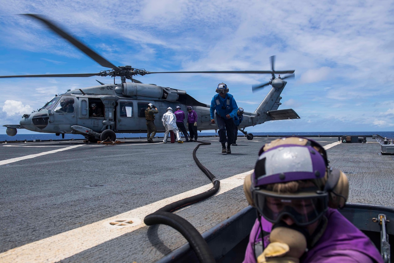 Sailors refuel a helicopter aboard a ship.