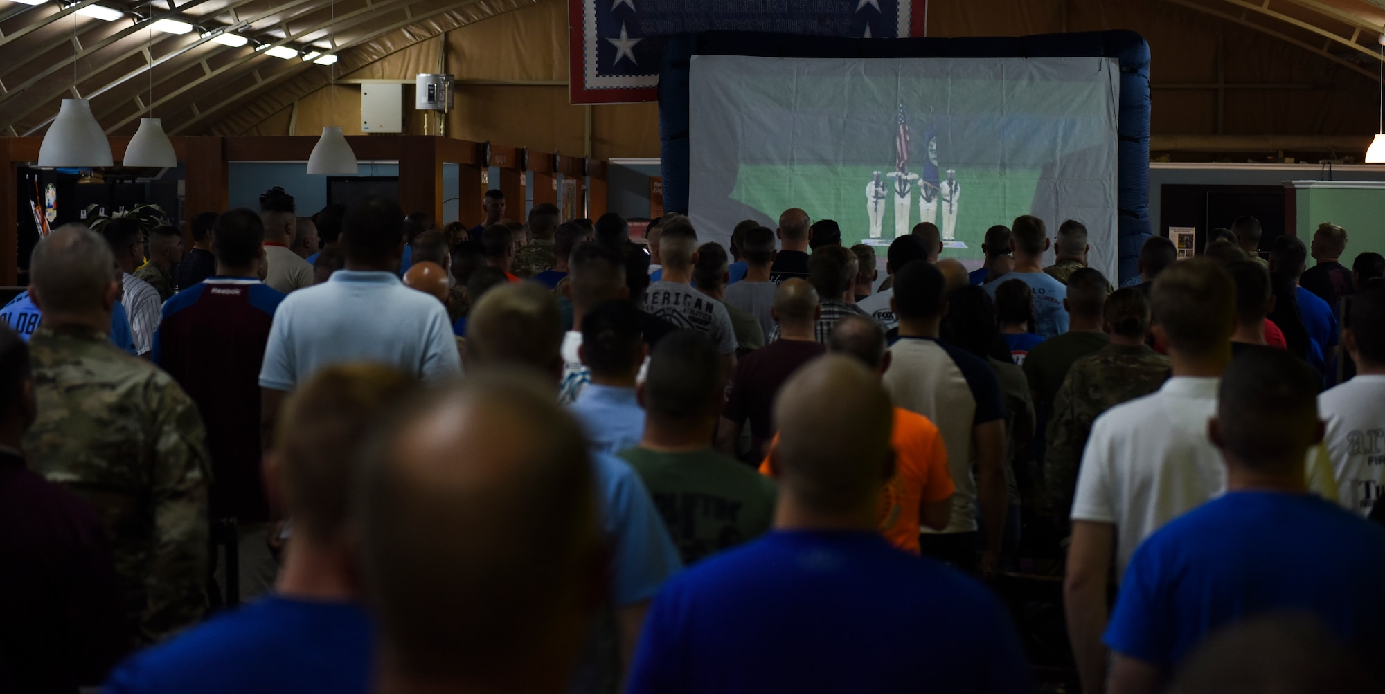 Service members stand for the playing of the National Anthem during the live-stream playing of a Kansas City Royals and Chicago White Sox game during the USO tour “This one’s for you” Sept. 12, 2018, at Camp Buehring, Kuwait. Four Royals baseball legends George Brett, Bret Saberhagen, Reggie Sanders, and Mike Sweeney were present to watch the game with the service members during their visit. (U.S. Air Force photo by Tech. Sgt. Caleb Pierce)