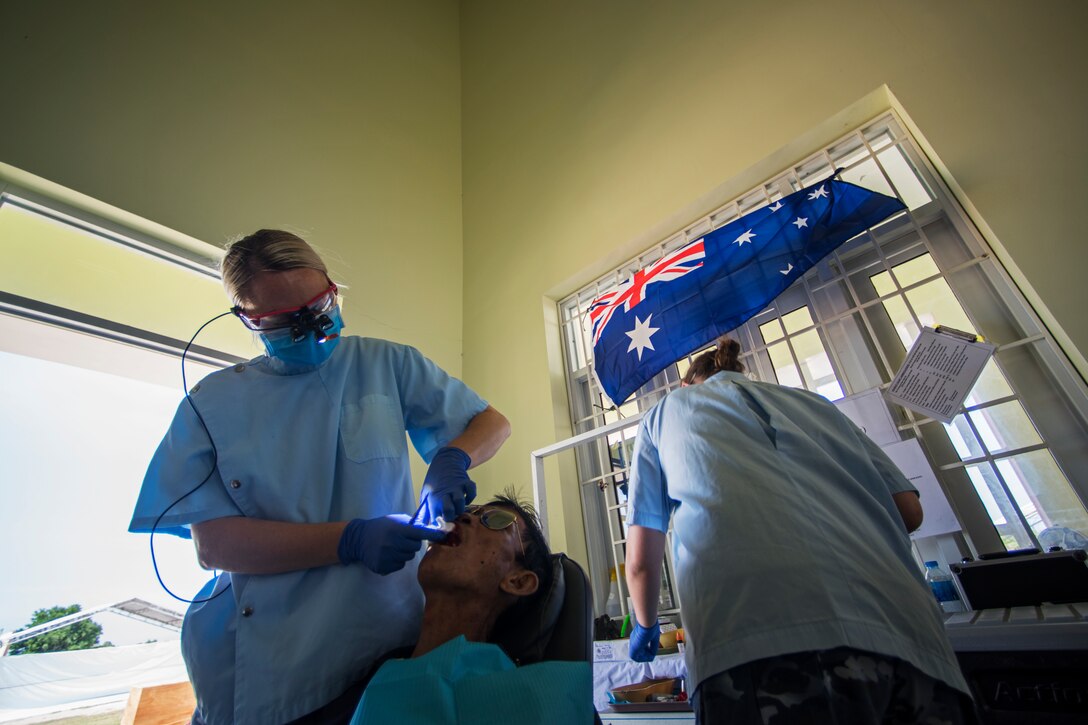 (Left) Royal Australian Air Force Flight (RAAF) Lieutenant Jess Raine,  RAAF dentist works with RAAF Cpl. Hannah Fortington, a senior dental assistant, to perform a tooth extraction on Luong Van Kiem during Pacific Angel (PAC ANGEL) 18-2 at the Cultural House of Tam Giang commune in Nui Thanh, Quang Nam province, Vietnam, Sept. 12, 2018.