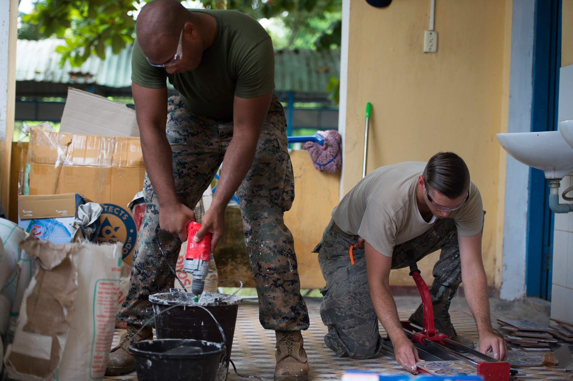 (Left) U.S. Marine Corps Sgt. David Tyson, 7th Engineer Support Battalion combat engineer, mixes grout as U.S. Air Force Staff Sgt. Zach Julian, 145th Airlift Wing water and fuel system maintenance craftsman, cuts tile during Pacific Angel (PAC ANGEL) 18-2 at Nguyen Hien Junior High School in in Phu Thinh town, Phu Ninh district, Vietnam, Sept. 11, 2018.