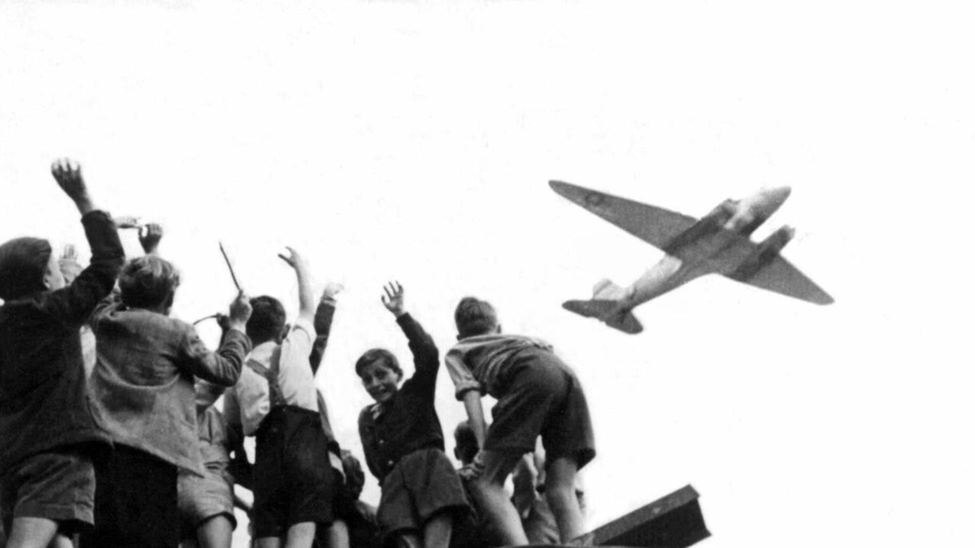 German children in West Berlin wave to an Air Force transport aircraft as it comes in to land at Templehof Airport during "Operation Vittles," better known as the Berlin Airlift in 1948. The USAF and United Kingdom Royal Air Force aircraft flew around the clock throughout the year and into 1949 when the Soviets reopened land routes on May 12. (U.S. Air Force photo)
