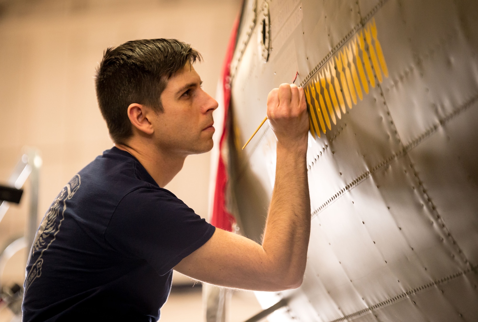 Museum restoration specialist Casey Simmons paints yellow silhouettes of bombs representing completed missions on the fuselage of the Boeing B-17F "Memphis Belle" during the restoration of the historic aircraft at Wright-Patterson Air Force Base, Ohio, Feb. 1, 2018. (U.S. Air Force photo by J.M. Eddins Jr.)