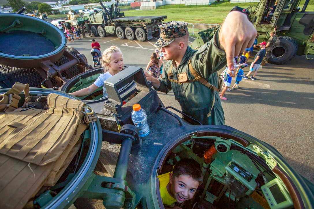 A Marine talks to children in a military vehicle.