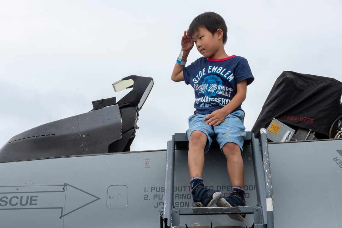 A child sits and salutes atop a static display at the 2018 Japanese-American Friendship Festival at Yokota Air Base, Japan, Sept. 15, 2018.