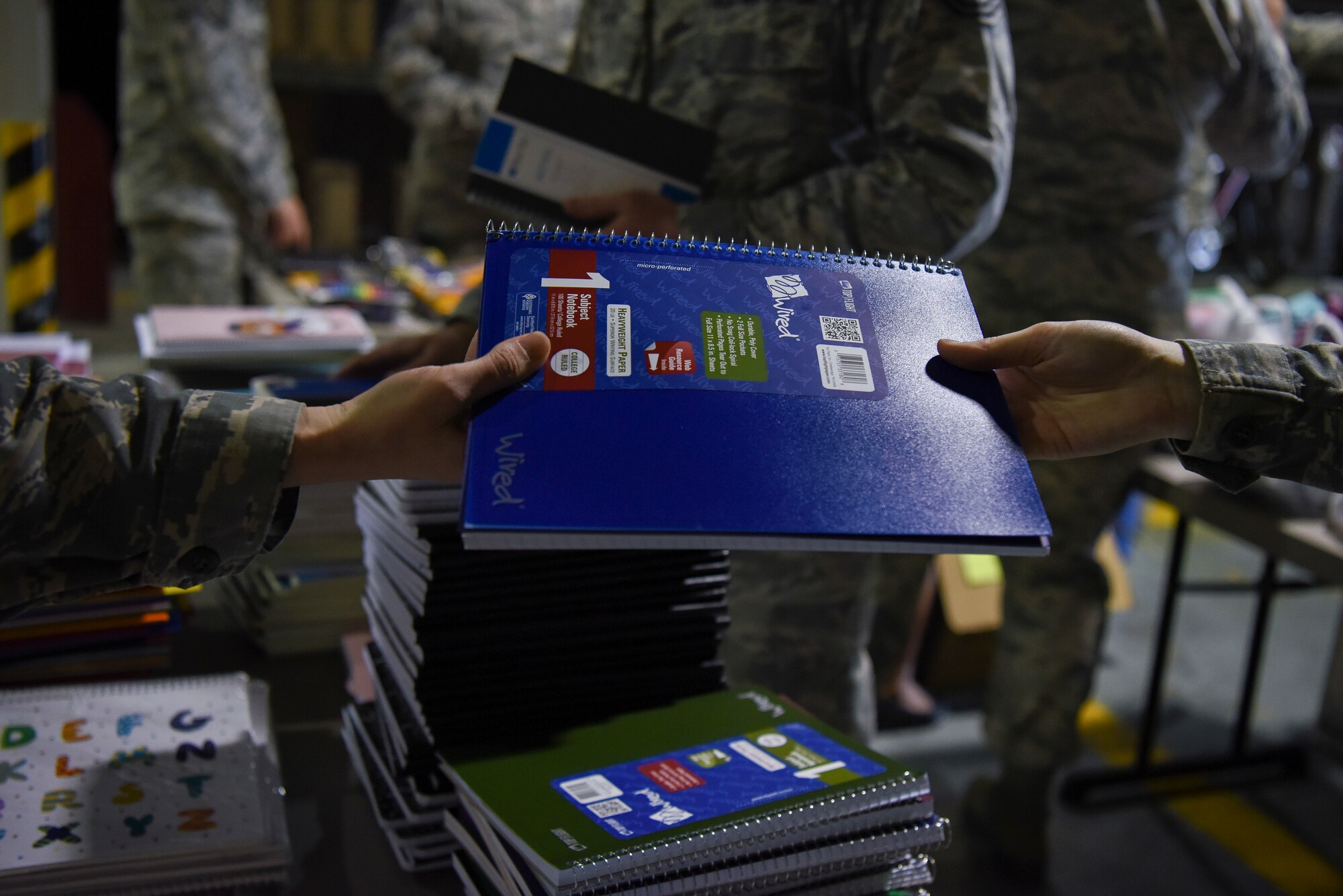 U.S. Air Force Airman 1st Class Katherine Bruner (right), 8th Logistics Readiness Squadron individual protective equipment technician, hands a notebook to Tech. Sgt. Kayla Rosensteil (left), 8th LRS flight service center noncommissioned officer in charge, at Kunsan Air Base, Republic of Korea, Sept. 13, 2018. The Back to School Drive received more than 5,000 dollars in donations for local schools. (U.S. Air Force photo by Senior Airman Savannah L. Waters)