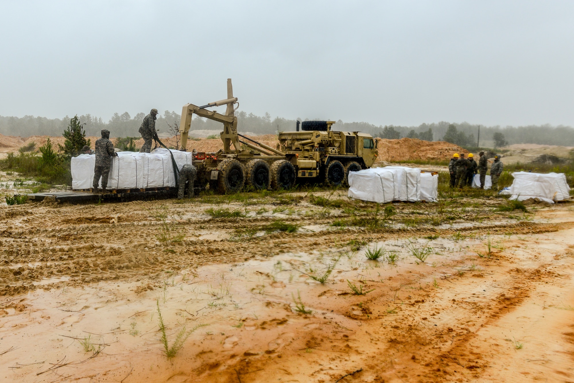 Soldiers use heavy equipment to fill large sandbags.