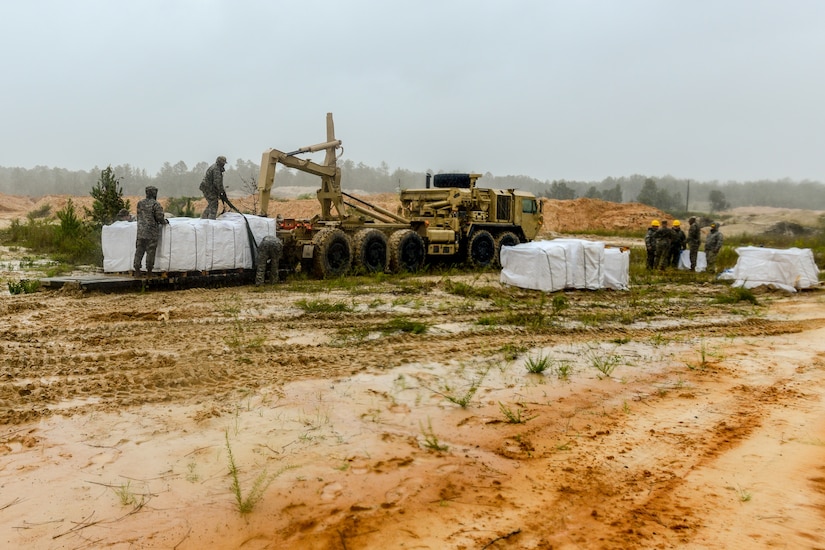 Soldiers use heavy equipment to fill large sandbags.