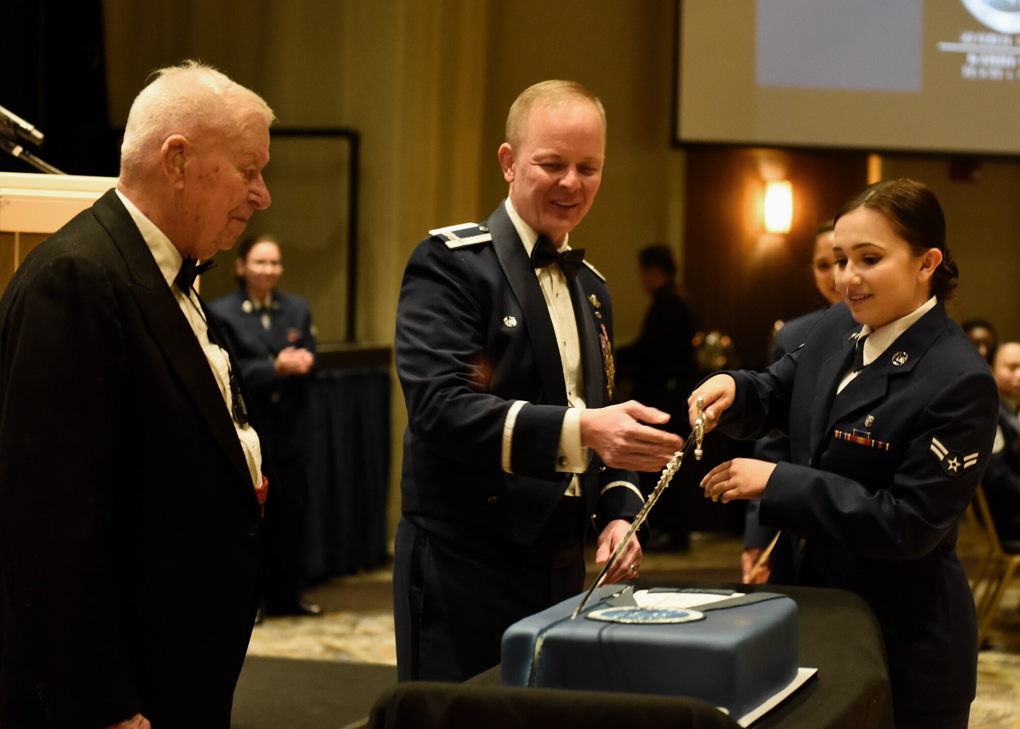 Col. Derek Salmi, 92nd Air Refueling Wing commander, assists the youngest attending Airman during a cake cutting ceremony at Fairchild's Air Force Ball at Northern Quest Resort and Casino in Airway Heights, Washington, Sept. 15, 2018. As part of the cake cutting tradition, a ceremonial saber is used to cut the cake by the youngest Airman . (U.S. Air Force photo/Airman 1st Class Lawrence Sena)
