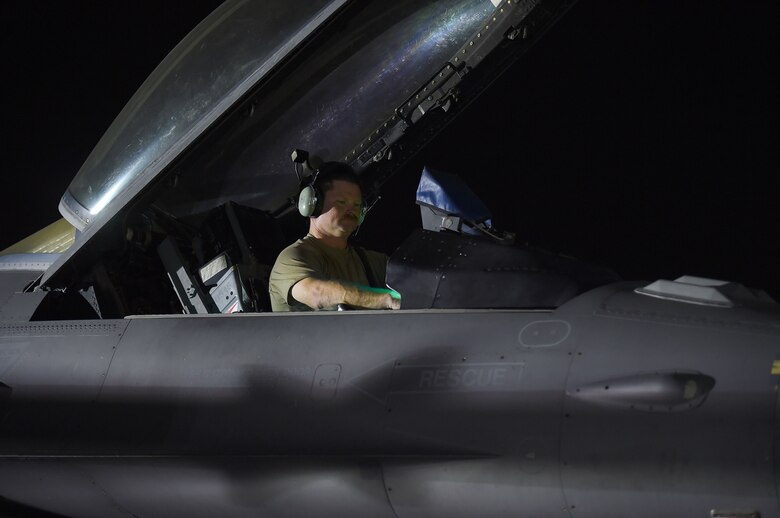 A crew chief sits in the cock pit of a fighter jet at night