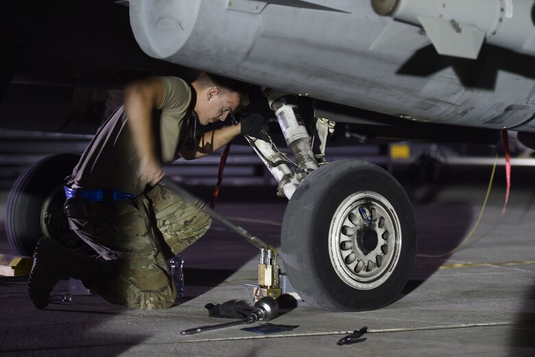 An Airman changes a tire on a jet at night