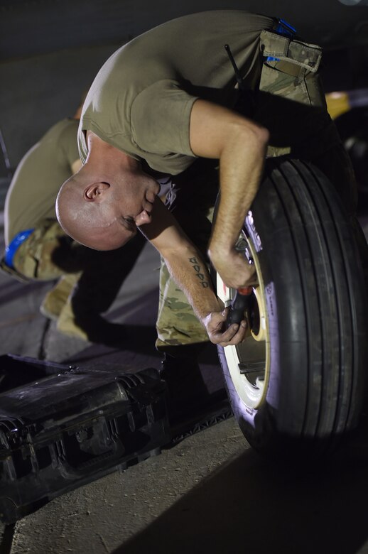 An Airman changes a tire on a jet at night