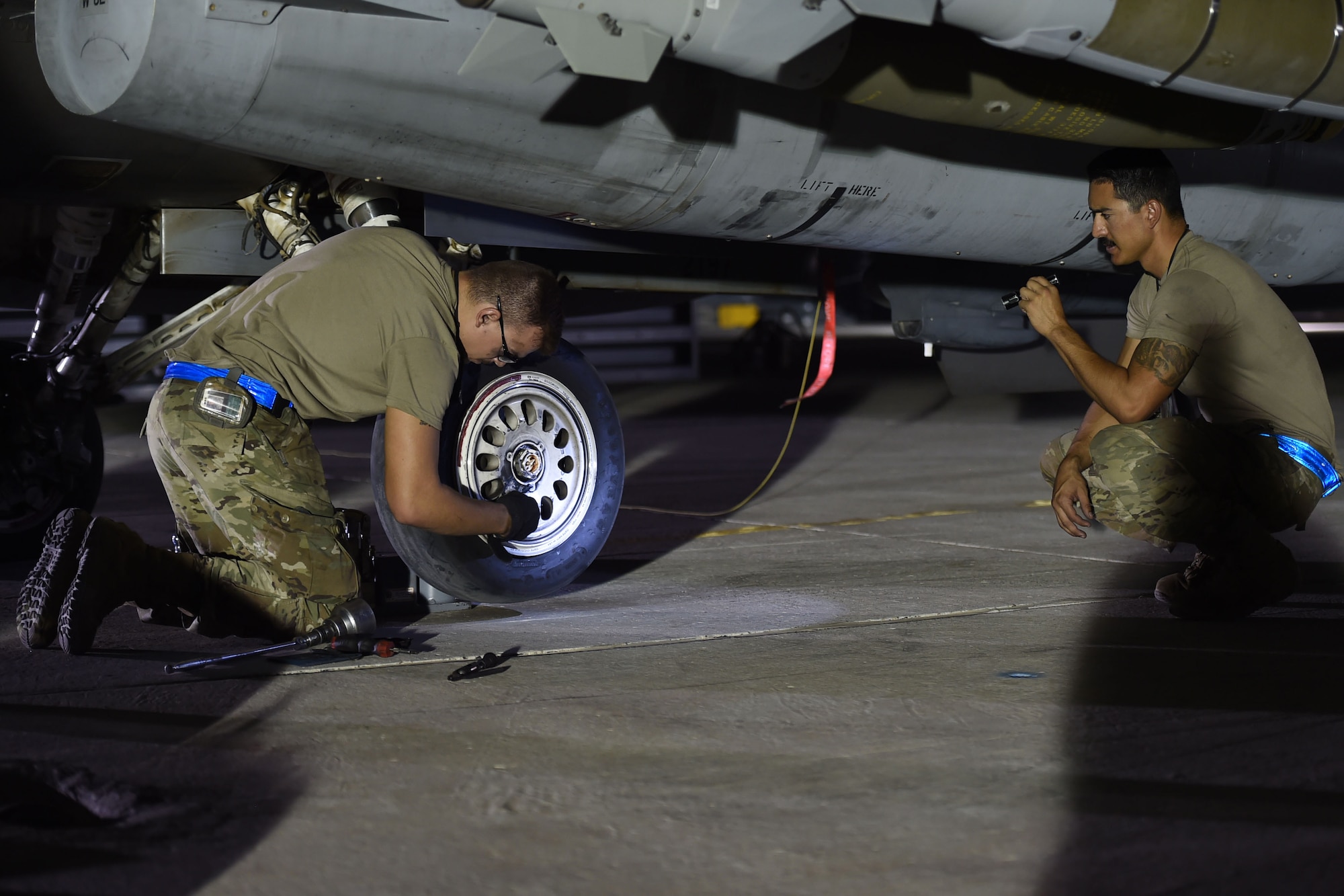 Two Airmen change a tire on a jet at night.