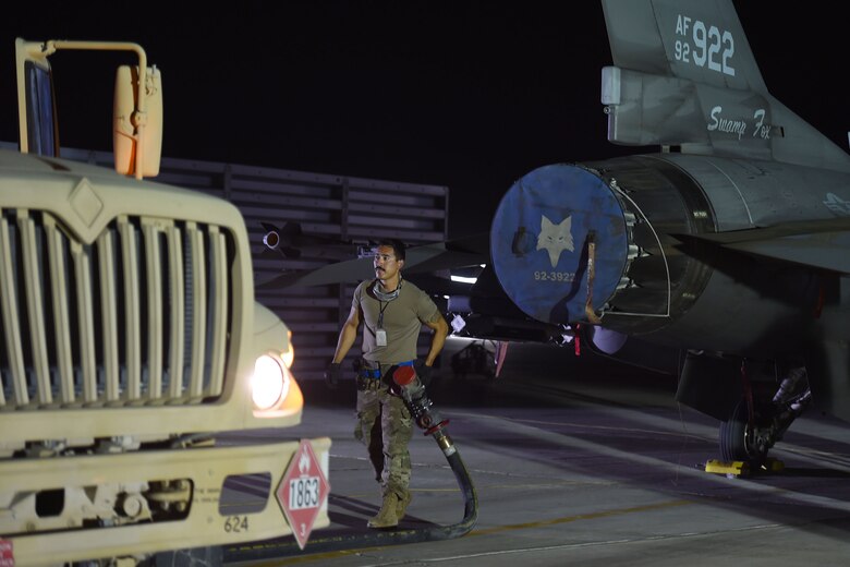 An Airmen carriers a big hose away from a jet
