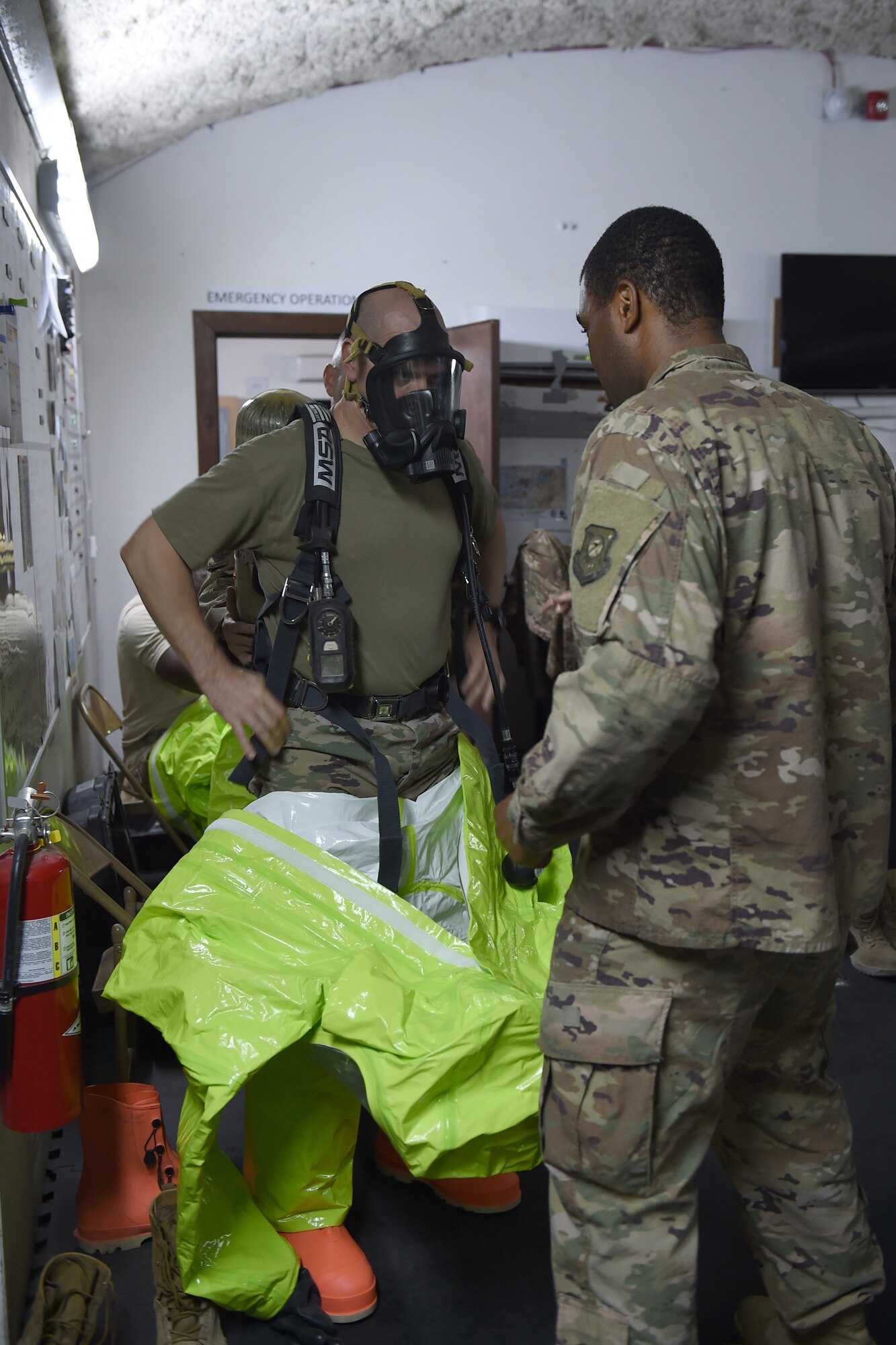 An Airman helps another Airman put on protection suit