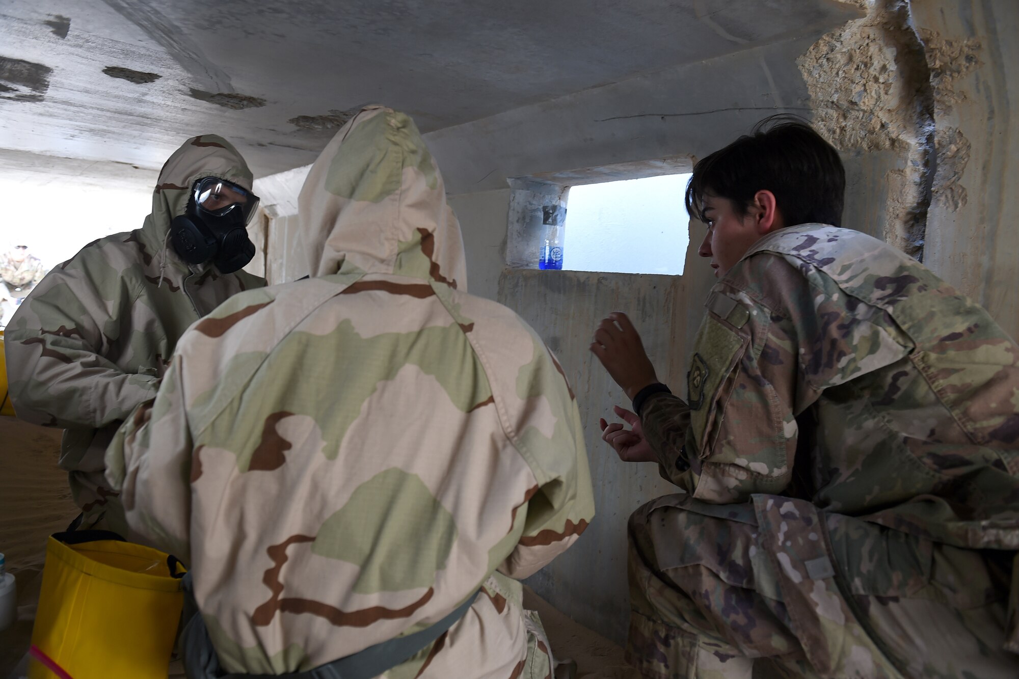 An Airman in chemical protection gear collects a sample of a liquid
