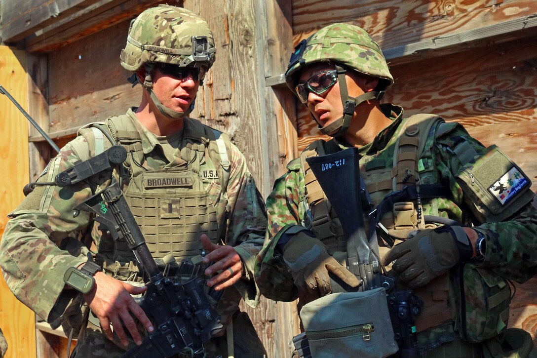 A U.S. and Japanese soldier talk training tactics before submitting their status report.