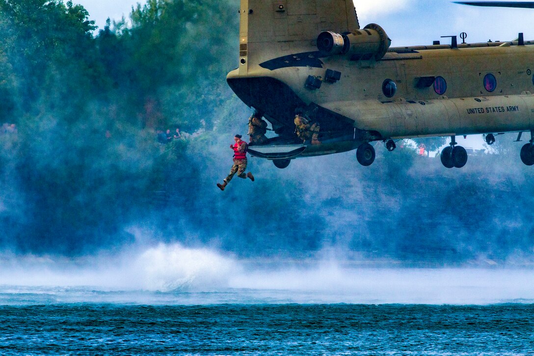 Soldiers jump from a helicopter into a lake.