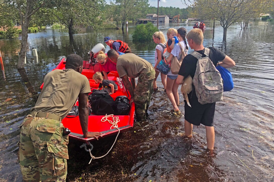 Guardsmen assist several residents into a boat during flooding.