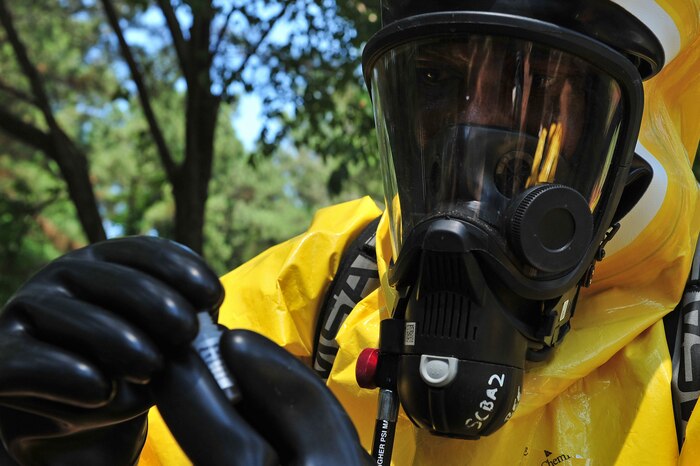 An airman in a bio suit holds up a sample in a tube.